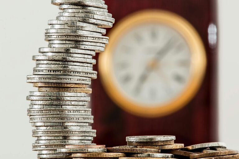 Stack of silver coins in front of a blurred clock symbolizing time and money