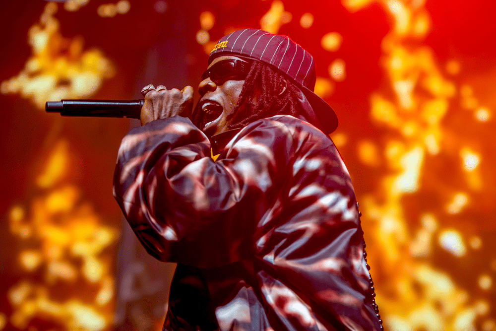 A high-energy photo of Rema mid-performance at a packed Afrobeat concert in early 2025, reflecting his global influence.